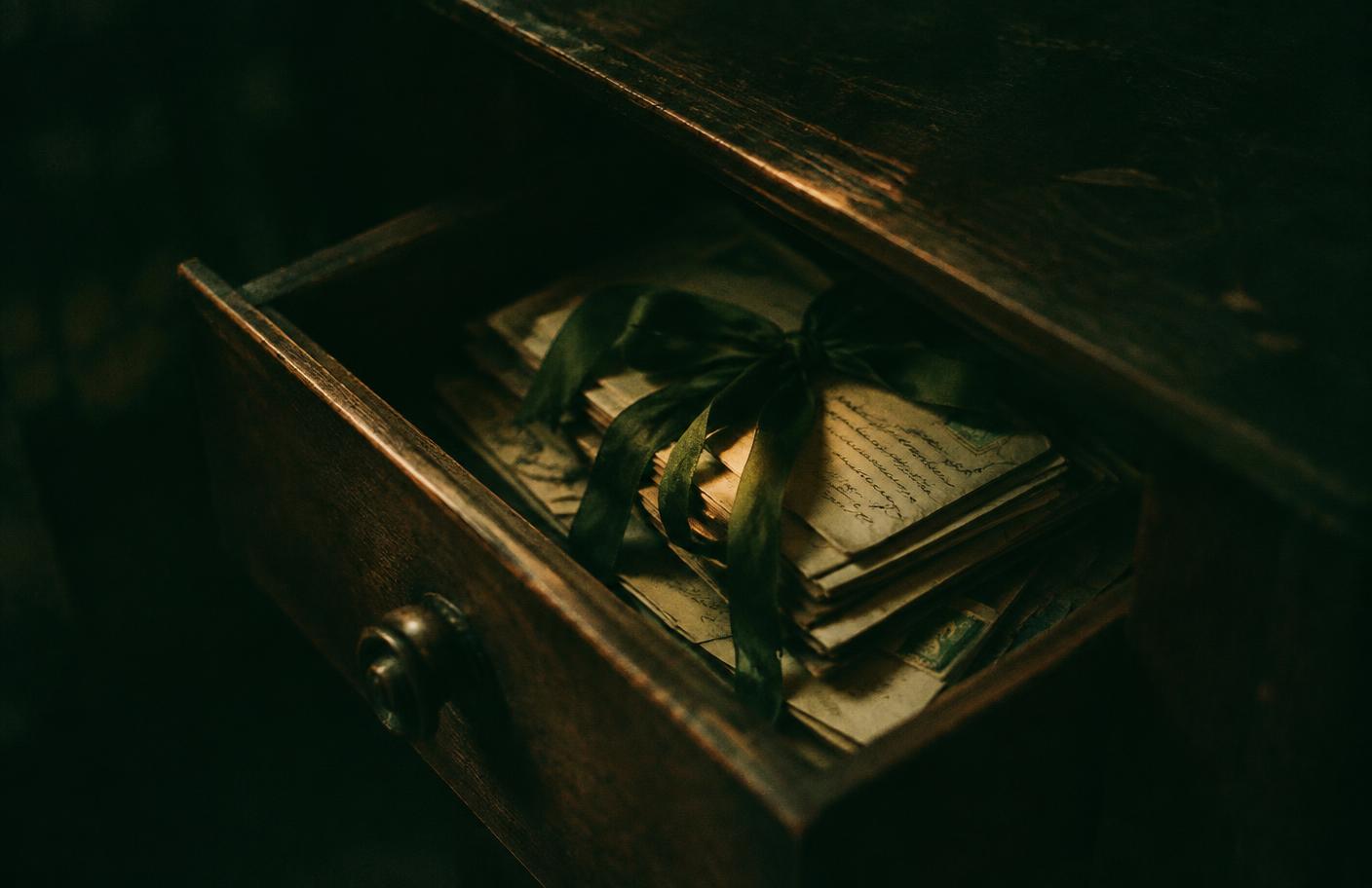 An old wooden drawer, slightly open, with letters tied in a loosened ribbon